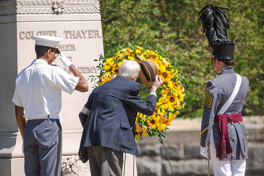 Old Grad Tipping Straw Hat alongside two cadets near Colonel Thayer Statue